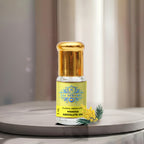 A premium glass vial of pure Mimosa Absolute Oil by Sai Perfume, gently resting on a bed of fluffy, golden-yellow Acacia dealbata blossoms.